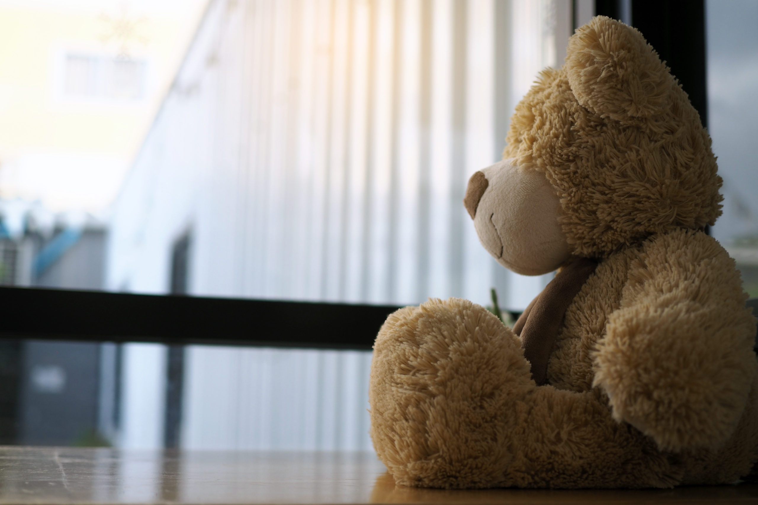 Child concept of sorrow. Teddy bear sitting leaning against the wall of the house alone, look sad and disappointed.